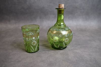 une bouteille en verre vert munie d'un bouchon en liège, à côté d'un verre à shot