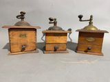 three antique wooden coffee grinders with brass handles and knobs