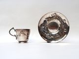 silver cup and saucer with a dragon design on the rim