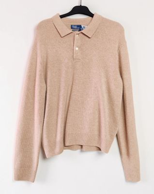 un pull beige suspendu à un cintre sur un mur blanc