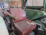 an old green truck with a red seat and a steering wheel