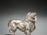 an antique silver figurine of a lion on a gray surface