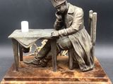 statue of a man sitting at a table with a candle in his hand