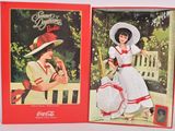 deux poupées Coca-Cola représentant des femmes en robe et chapeau, assises sur un banc