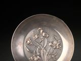 an antique silver plate with flowers on it on a black surface