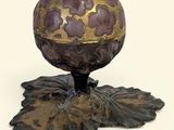 un œuf violet et doré posé sur un socle orné de feuilles