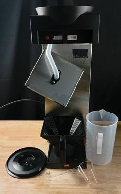 une cafetière posée sur une table, avec une tasse à côté
