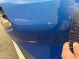 a person holding a measuring tape to measure the front of a blue car