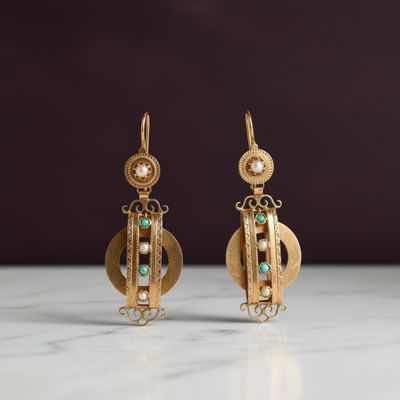 une paire de boucles d'oreilles en or ornées de perles et d'émeraudes, posées sur une surface en marbre