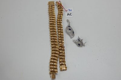 deux bracelets en or et une chaîne munie d'un fermoir, posés sur un fond blanc