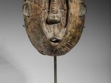 un masque en bois posé sur un socle métallique, sur fond blanc