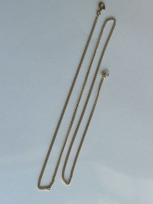 un gros plan d'un collier en argent avec une chaîne, posé sur une surface blanche