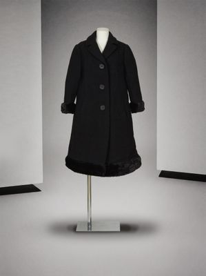 un manteau noir posé sur un pied de mannequin dans une pièce blanche