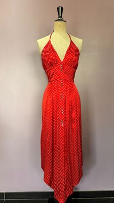 une robe rouge posée sur un mannequin adossé à un mur