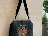un sac à main noir orné de broderies florales, accroché au mur à côté d'une plante en pot