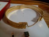 un bracelet en or orné d'une pierre verte, à côté d'une boîte rouge
