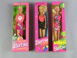 three barbie dolls are in a pink box on a gray surface