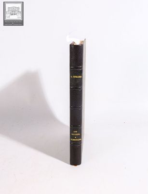 an old black book sitting on top of a table next to a white wall