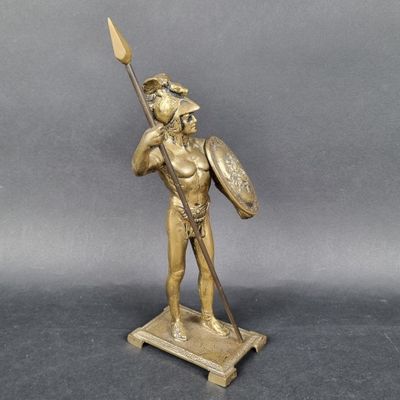une statue antique en bronze représentant un homme tenant une lance et un bouclier