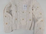 Le pull est blanc et orné de boutons dorés.