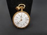 une petite montre de poche en or exposée sur un socle noir