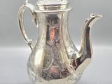 une théière ancienne en argent avec son couvercle, posée sur une table