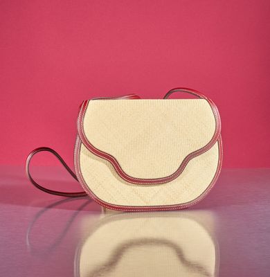 beige and red purse on a table against a pink background