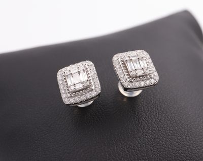 a pair of white gold and diamond earrings on a black leather surface