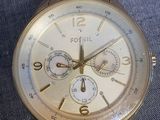 gold fossil watch on a blue cloth with a white background