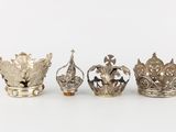four silver crowns are lined up in a row on a white surface