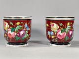 pair of red vases with floral designs on them sitting on a table