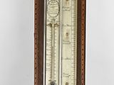a tall wooden clock with a barometer on top of it
