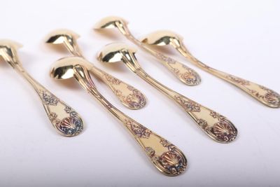 six gold spoons with floral designs on them sitting on a white surface