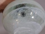 a person holding a glass vase with a green marble inside of it