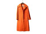 un manteau orange suspendu à un cintre sur un mur blanc