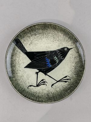 une petite assiette sur laquelle est représenté un oiseau, posée sur une table