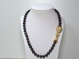 collier en perles noires et dorées orné d'un pendentif en forme de feuille dorée