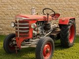 un tracteur rouge garé dans l'herbe près d'un mur de briques