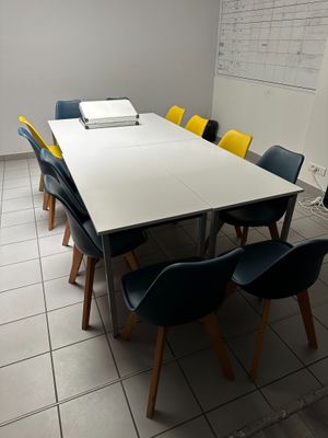 des chaises aux couleurs vives disposées autour d'une table blanche dans une pièce où se trouve un tableau blanc accroché au mur