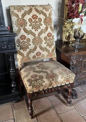 une chaise dont l'assise est recouverte d'un tissu à motifs floraux, à côté d'une table sur laquelle se trouve un vase de fleurs