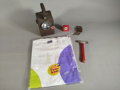 une photo représentant un appareil photo, un t-shirt et une paire de ciseaux posés sur une table