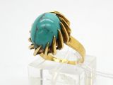 Bague en or et pierre turquoise, posée sur un socle en acrylique transparent