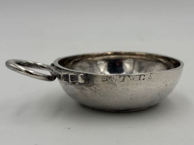une coupe ancienne en argent munie d'une anse, posée sur une surface blanche