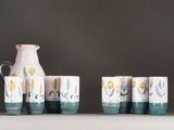 five cups and a jug sitting on a shelf next to each other