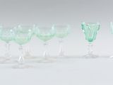 several green wine glasses are lined up on a white surface