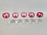 four wine glasses with pink designs are lined up on a white surface