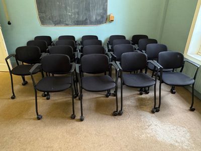 rows of black chairs in a room with a chalkboard on the wall