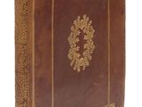un vieux livre marron avec des bordures dorées posé sur une surface blanche
