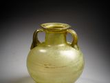 un vase en verre jaune posé sur une surface blanche, sur fond noir