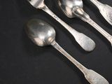 quatre cuillères en argent et une fourchette posées sur un fond noir